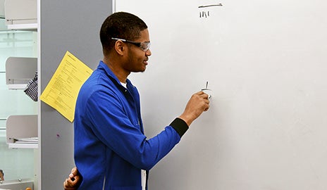 Teaching assistant writing equation on a whiteboard.