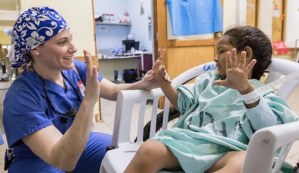 A smiling doctor and youngster compare the spread of their fingers.