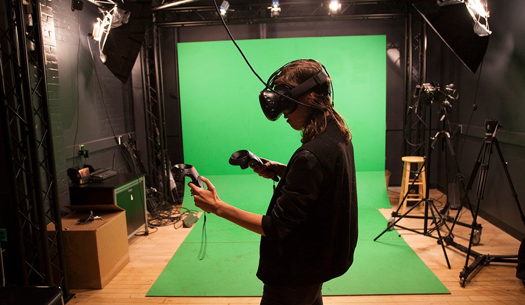 A young woman wearing a virtual reality headset in front of a green screen. 