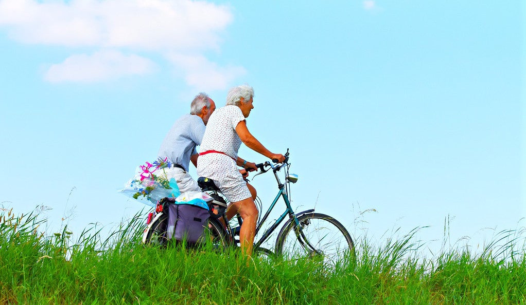 An elderly man and woman riding bikes in a field. 