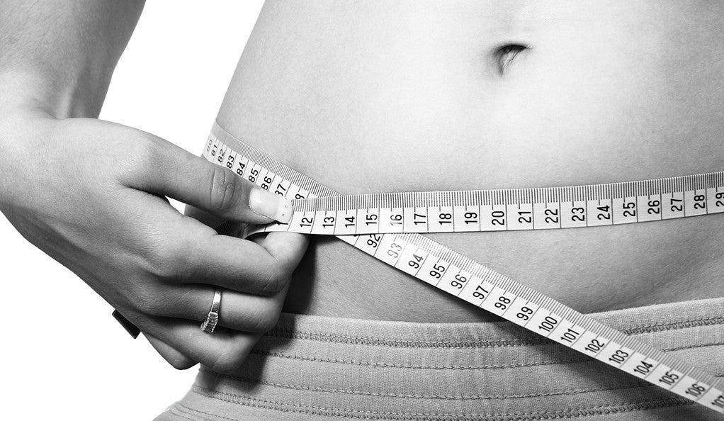 A black and white photo of a woman measuring her belly with tape.