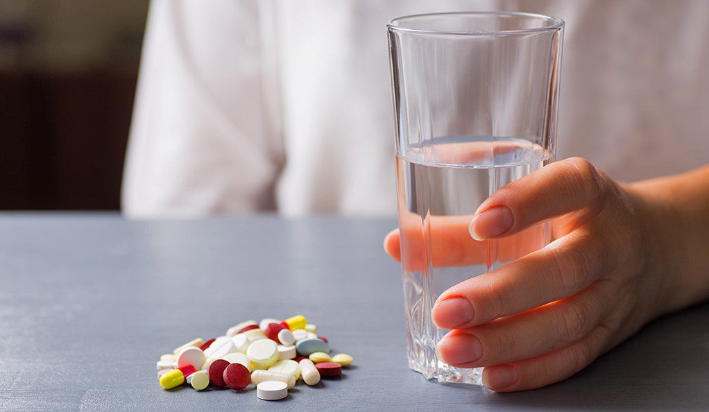 A person holding a glass of water next to a pile of prescription pills.