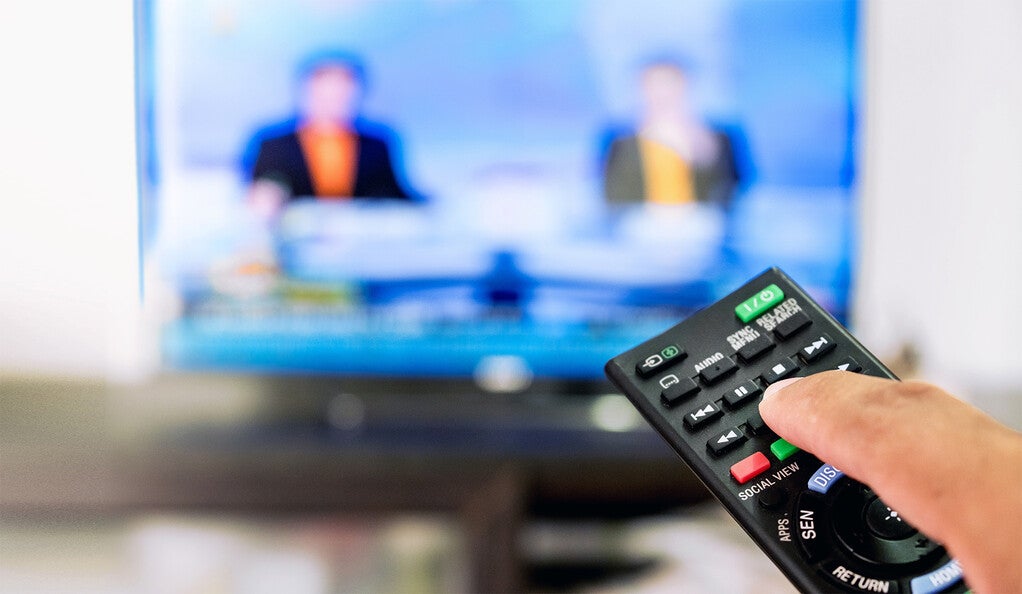A person pointing their remote at the TV while the news is on
