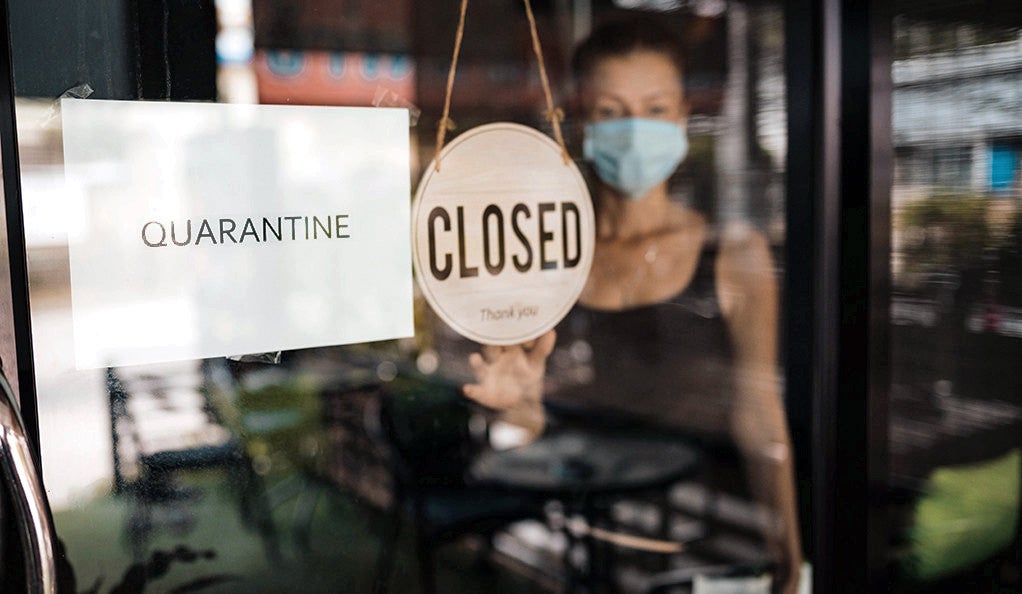 Shop owner in a surgical mask hanging a closed sign on the door of her business.