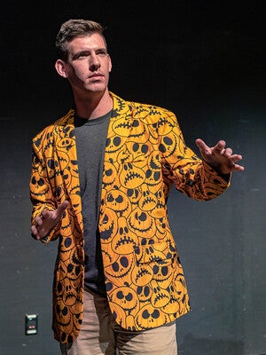 Man wearing an orange jacket with carved pumpkin faces.