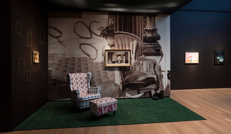A tableau with an upholstered chair, green carpet, and framed photographs.