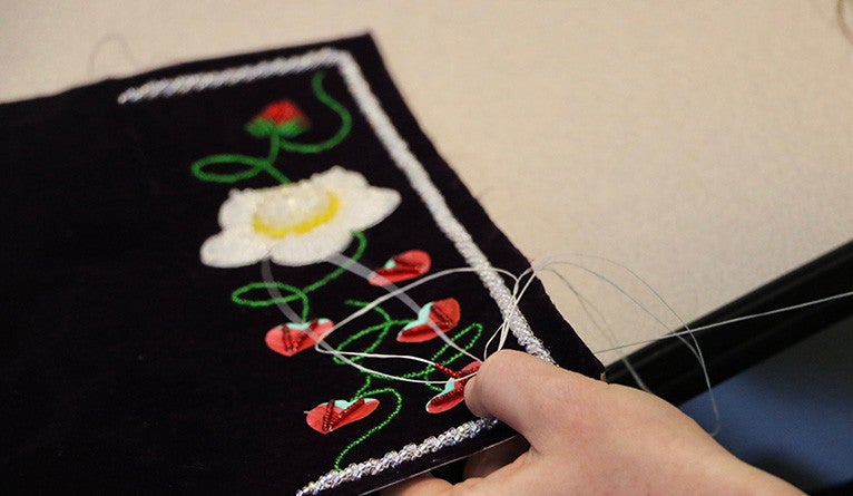 A person’s hands as they sew a raised beadwork piece. 